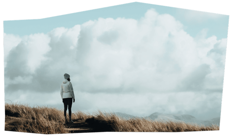 Ein Foto von einer Frau, die auf einem Berg steht und in die Ferne schaut.